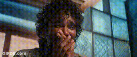 A Man With Curly Hair Is Covering His Mouth With His Hands In A Room . GIF