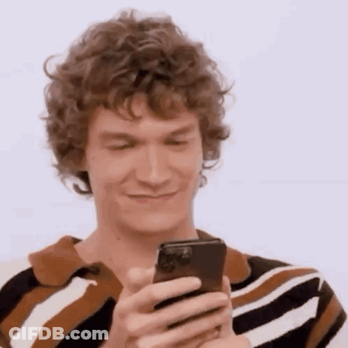 A Man With Curly Hair Is Holding A Cell Phone In His Hand . GIF