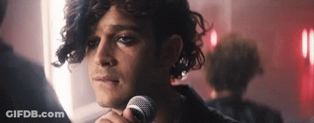 A Man With Curly Hair Is Holding A Microphone In His Hand . GIF
