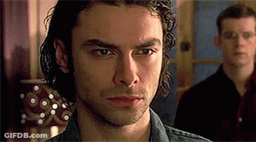 A Man With Curly Hair Is Looking At The Camera While Another Man Stands Behind Him . GIF