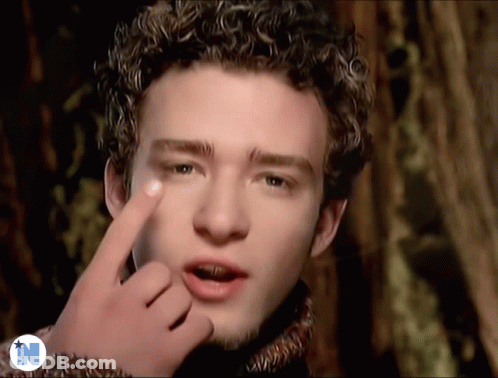 A Man With Curly Hair Is Making A Funny Face With His Finger GIF