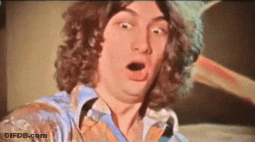 A Man With Curly Hair Is Making A Surprised Face With His Mouth Open GIF