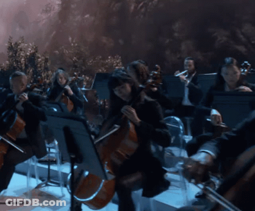 A Man With Curly Hair Is Playing A Flute In Front Of An Orchestra GIF