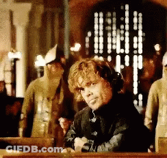 A Man With Curly Hair Is Sitting At A Table In Front Of A Window GIF