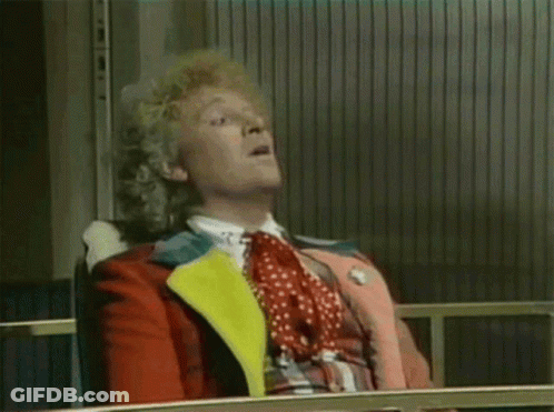 A Man With Curly Hair Is Sitting In A Chair And Making A Funny Face . GIF