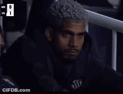 A Man With Curly Hair Is Sitting In A Stadium Watching A Game With The Score Bar 0 Leg 1 GIF