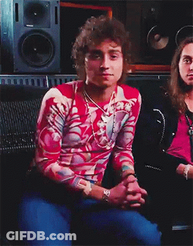 A Man With Curly Hair Is Sitting In Front Of A Speaker GIF
