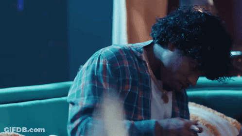 A Man With Curly Hair Is Sitting On A Couch Looking Down GIF