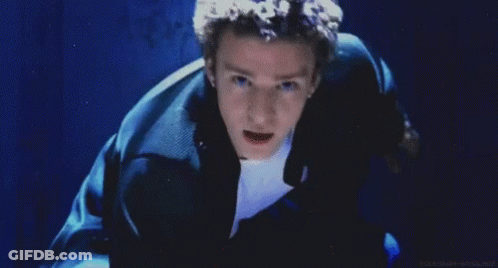 A Man With Curly Hair Is Smiling In Front Of A Blue Wall GIF