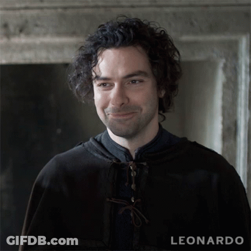 A Man With Curly Hair Is Smiling In Front Of A Leonardo Sign GIF