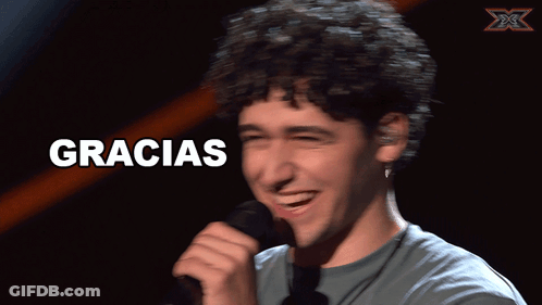 A Man With Curly Hair Is Smiling In Front Of A Sign That Says " Gracias " GIF