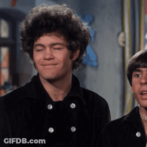 A Man With Curly Hair Is Smiling While Wearing A Black Jacket GIF