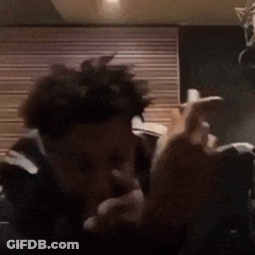 A Man With Curly Hair Is Smoking A Cigarette In Front Of A Wooden Wall . GIF