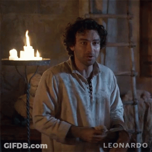 A Man With Curly Hair Is Standing In Front Of A Candle Holder With The Name Leonardo On The Bottom Right GIF