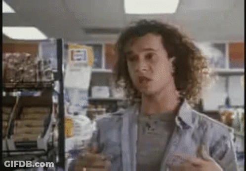 A Man With Curly Hair Is Standing In Front Of A Sign That Says ' E ' On It . GIF