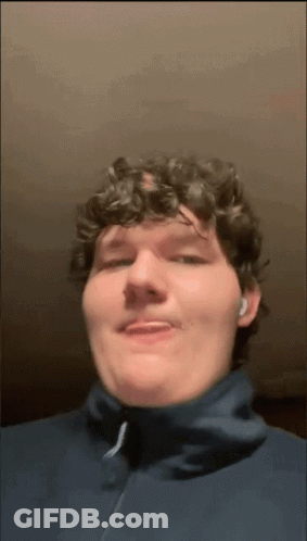 A Man With Curly Hair Is Wearing A Blue Jacket And Ear Buds GIF