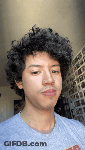 A Man With Curly Hair Is Wearing A Grey Shirt That Says ' A ' On The Front GIF
