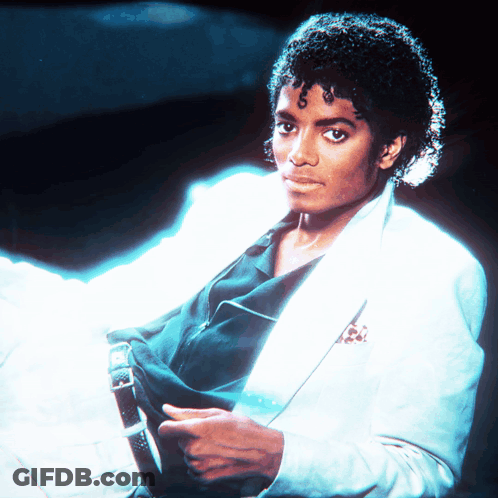 A Man With Curly Hair Is Wearing A White Jacket And Black Shirt GIF