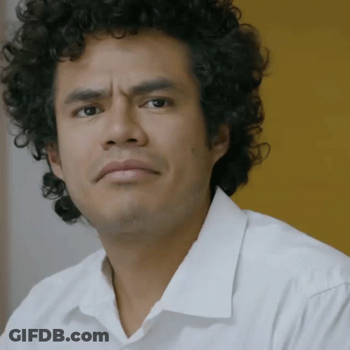 A Man With Curly Hair Is Wearing A White Shirt And Looking At The Camera GIF