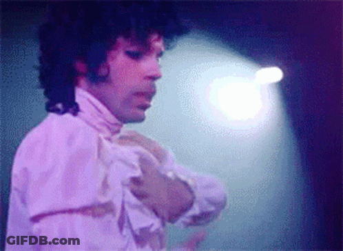 A Man With Curly Hair Is Wearing A White Shirt With Ruffles On The Sleeves GIF