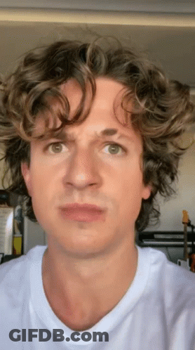 A Man With Curly Hair Is Wearing A White T-Shirt And Making A Funny Face GIF