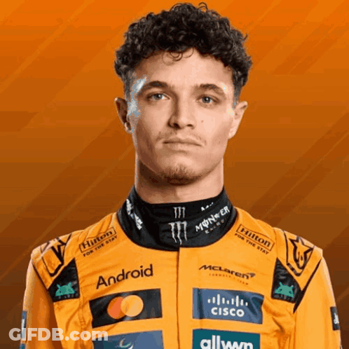 A Man With Curly Hair Is Wearing An Orange Racing Suit With Logos For Hilton And Cisco GIF