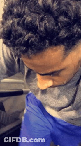 A Man With Curly Hair Is Wearing Blue Shorts And A Grey Shirt GIF