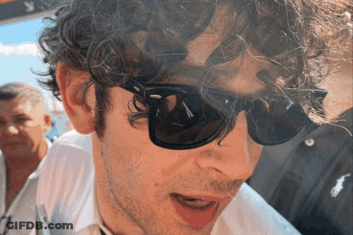 A Man With Curly Hair Is Wearing Sunglasses And A White Shirt GIF