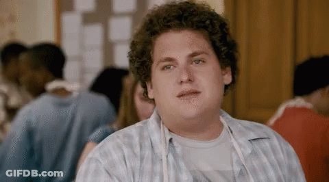 A Man With Curly Hair Looks At The Camera With A Group Of People In The Background GIF