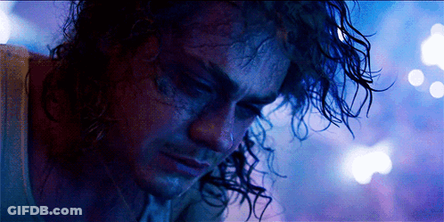 A Man With Curly Hair Looks Down At Something GIF