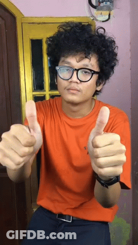 A Man With Curly Hair Wearing Glasses And An Orange Shirt Giving A Thumbs Up GIF