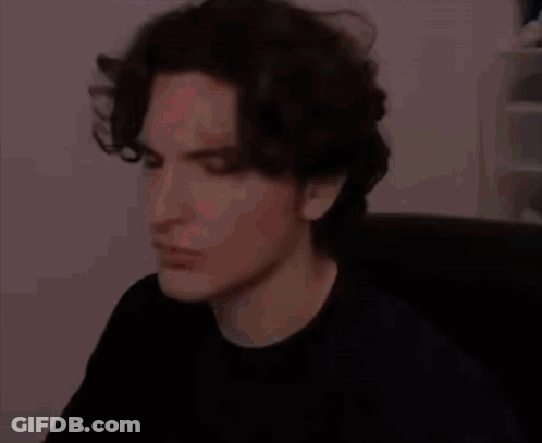 A Man With Dark Hair Is Sitting In A Chair And Making A Funny Face . GIF