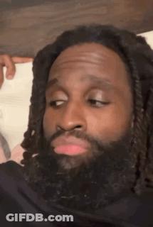 A Man With Dreadlocks And A Beard Is Making A Funny Face While Sitting On A Bed . GIF