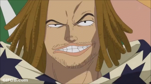 A Man With Dreadlocks And A Beard Is Smiling With A Flag In The Background GIF