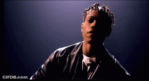 A Man With Dreadlocks And A Black Leather Jacket Looks At The Camera GIF