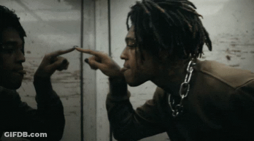 A Man With Dreadlocks And A Chain Around His Neck Looks At Himself In A Mirror GIF