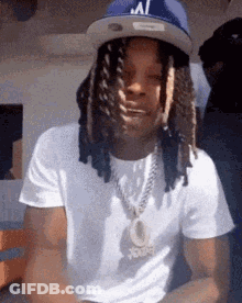 A Man With Dreadlocks And A Hat Is Wearing A White Shirt And A Chain . GIF