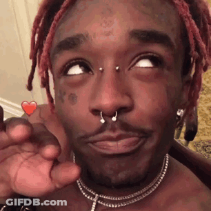 A Man With Dreadlocks And A Nose Ring Is Holding A Heart Shaped Candy In His Hand . GIF