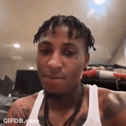 A Man With Dreadlocks And A Tattoo On His Chest Is Wearing A White Tank Top And A Necklace . GIF