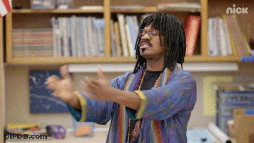 A Man With Dreadlocks And Glasses Is Standing In Front Of A Bookshelf With The Nick Logo On It GIF
