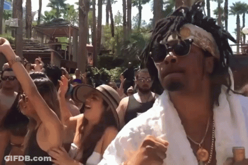 A Man With Dreadlocks And Sunglasses Is Dancing In Front Of A Crowd Of People GIF