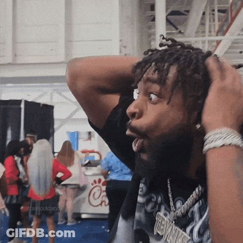 A Man With Dreadlocks Has His Hands On His Head And A Chick-Fil-A Sign In The Background GIF