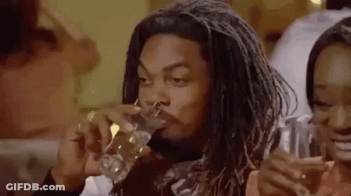 A Man With Dreadlocks Is Drinking A Glass Of Water While Sitting At A Table . GIF