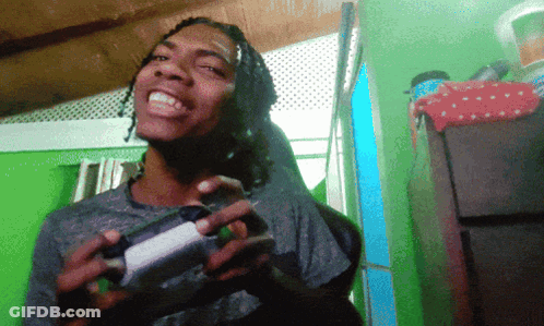 A Man With Dreadlocks Is Holding A Game Controller And Smiling GIF