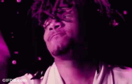 A Man With Dreadlocks Is Holding A Purple Object In His Hand And Making A Funny Face . GIF
