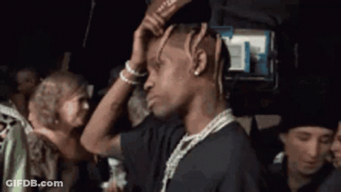 A Man With Dreadlocks Is Holding His Head While Standing In A Crowd Of People . GIF