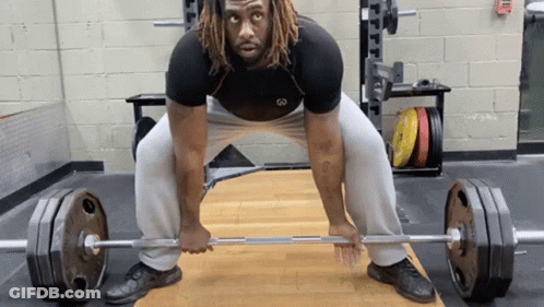 A Man With Dreadlocks Is Lifting A Barbell In A Gym . GIF