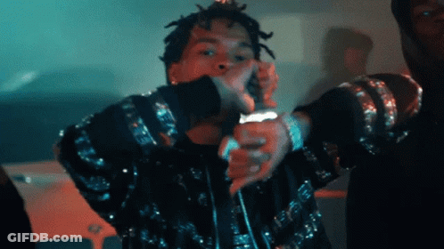 A Man With Dreadlocks Is Singing Into A Microphone While Wearing A Black Jacket GIF
