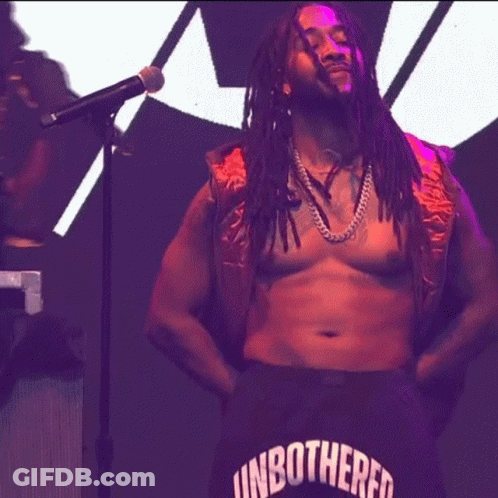 A Man With Dreadlocks Is Singing Into A Microphone While Wearing Shorts That Say Unbothered GIF