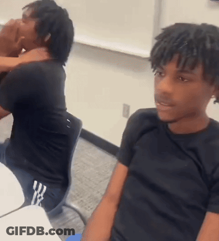 A Man With Dreadlocks Is Sitting At A Desk In A Classroom . GIF
